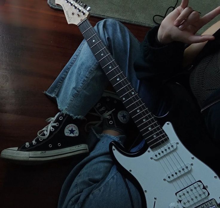 a person sitting on the floor with an electric guitar in front of them and pointing at something