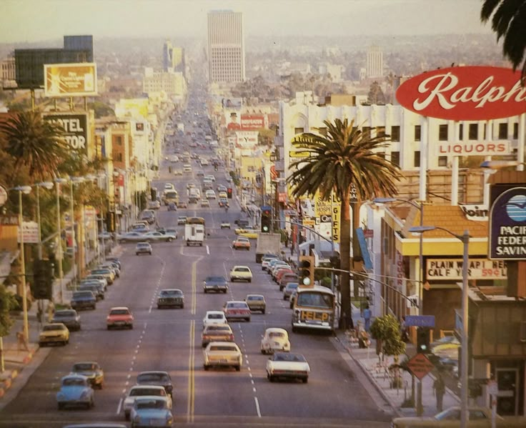 cars are driving down the road in front of buildings and palm trees on both sides