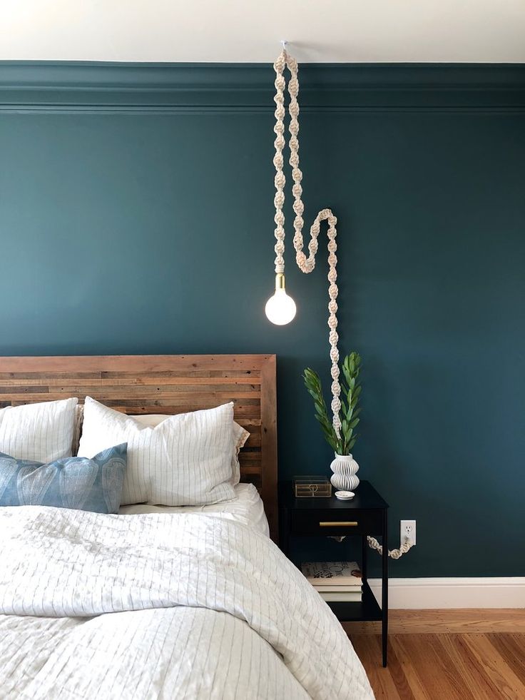 a bedroom with blue walls and white bedding, wooden headboard and lamp hanging from the ceiling