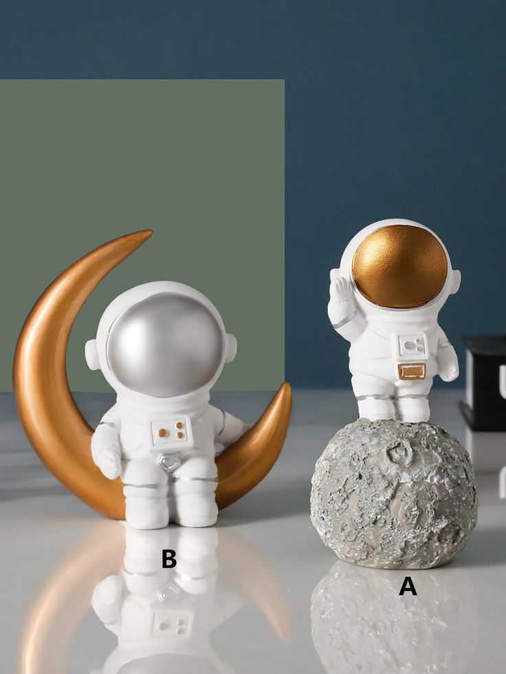 an astronaut doll sitting on top of a rock next to a moon and letter b