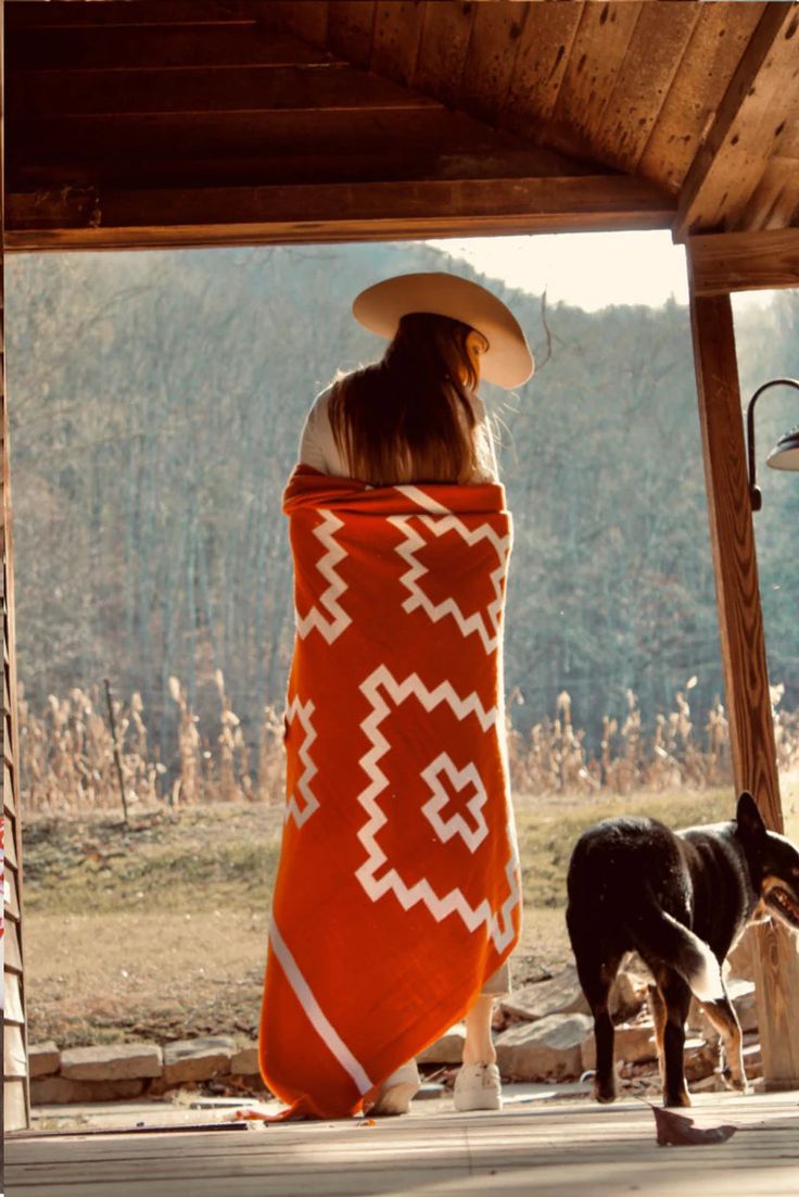 a woman wrapped in an orange blanket sitting on a porch next to a black and white cow