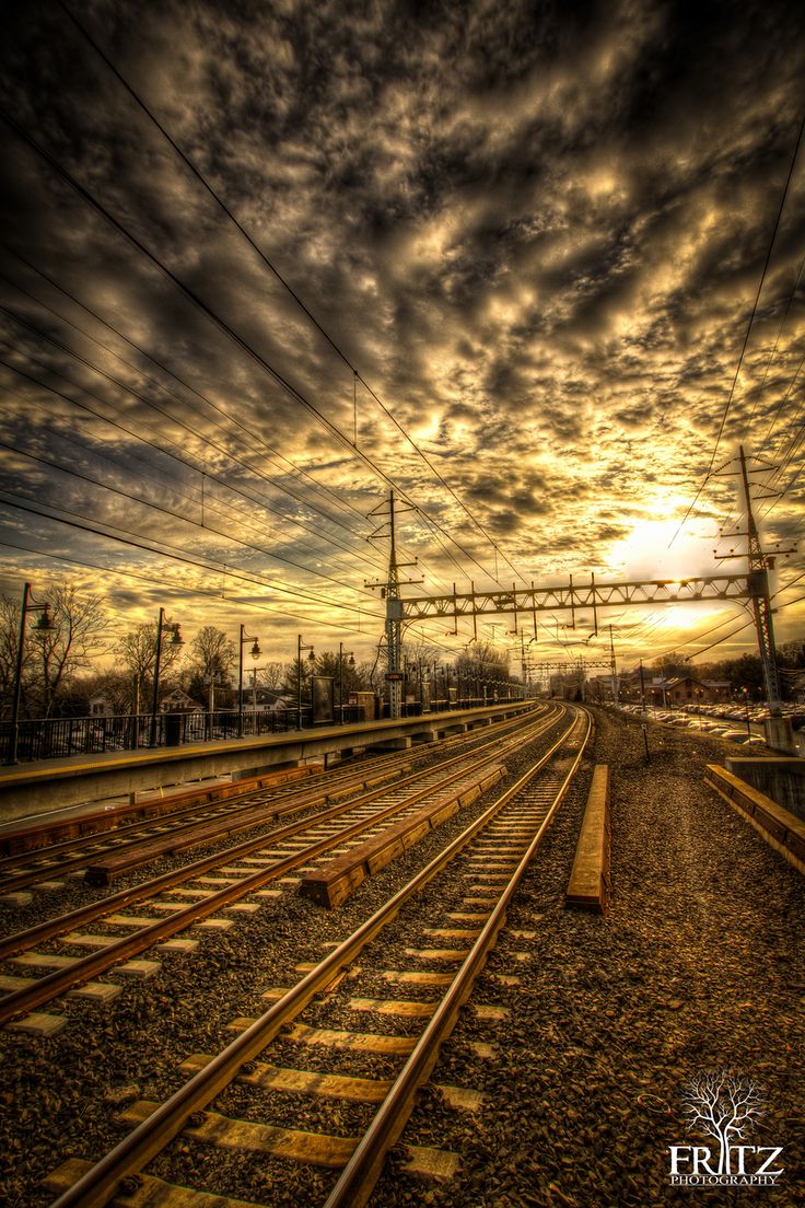 the sun is setting over train tracks in an empty area with power lines and telephone poles