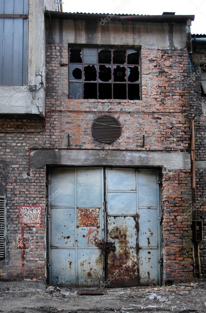 an old brick building with two blue doors and broken windows in the middle of it