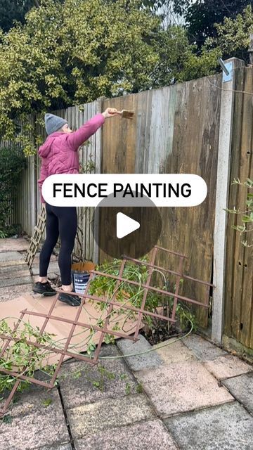 a woman in pink jacket painting a fence