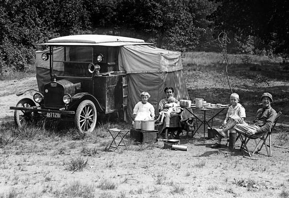 black and white photograph of people sitting in chairs around an old truck with a tarp on top