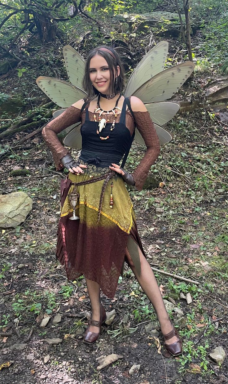 a woman dressed as a fairy standing in the woods with her hands on her hips