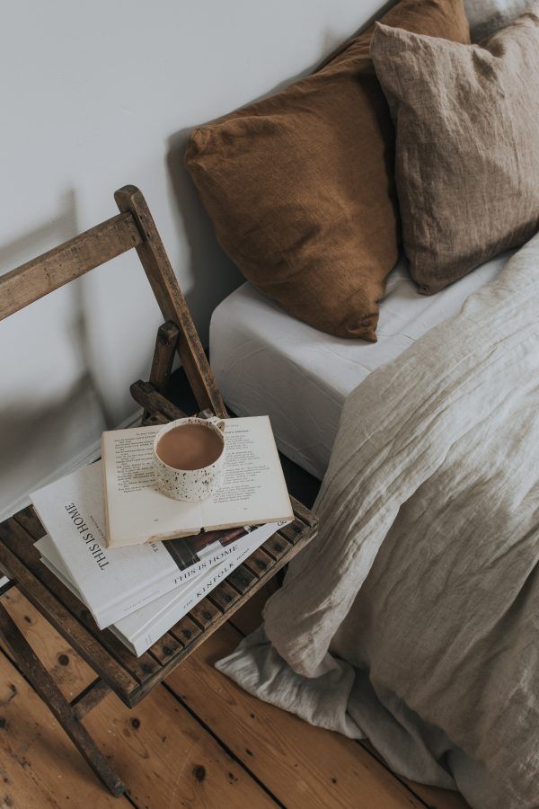 an open book on a table next to a bed with two pillows and a wooden chair