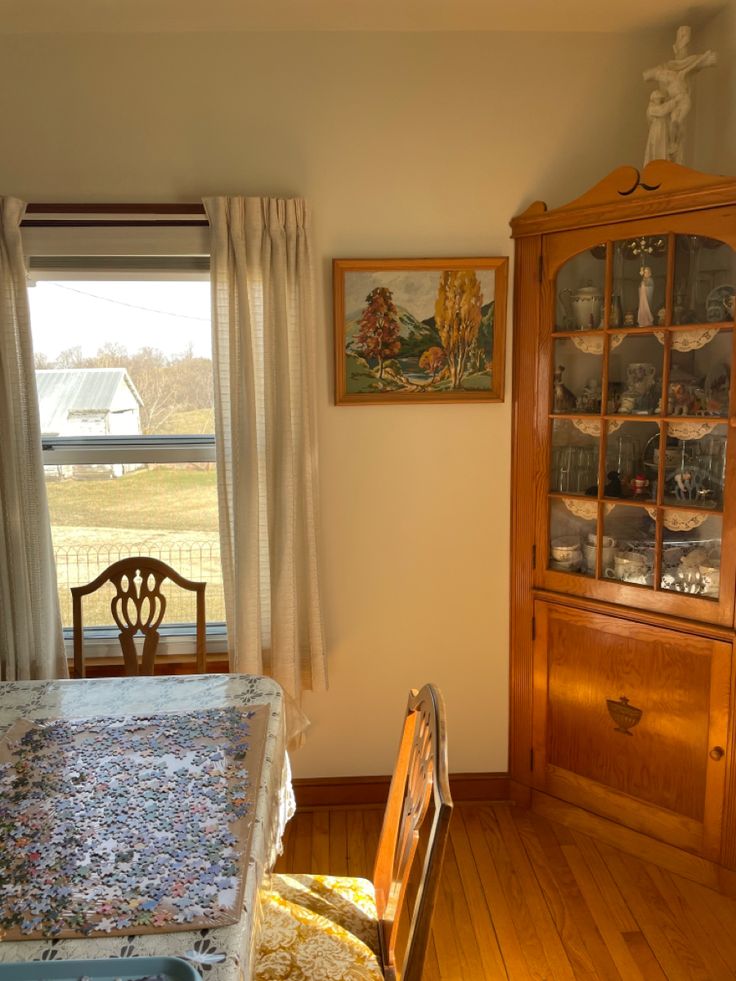 a room with a bed, china cabinet and table in it's corner next to a window