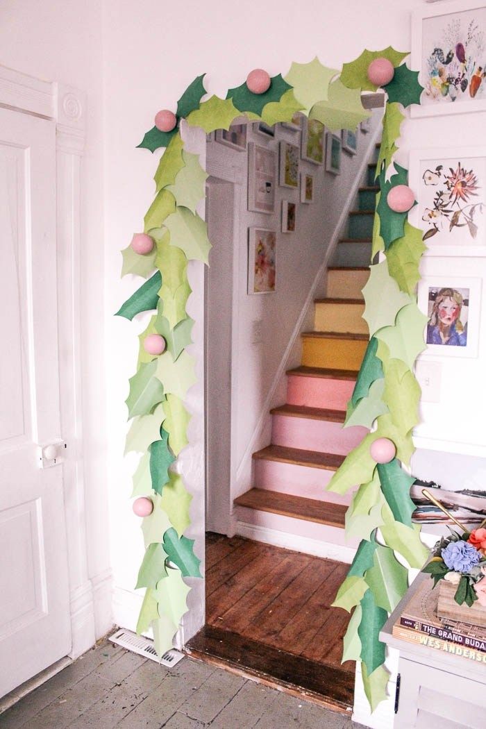 an arch made out of paper and decorated with holly leaves on the bottom, next to a staircase