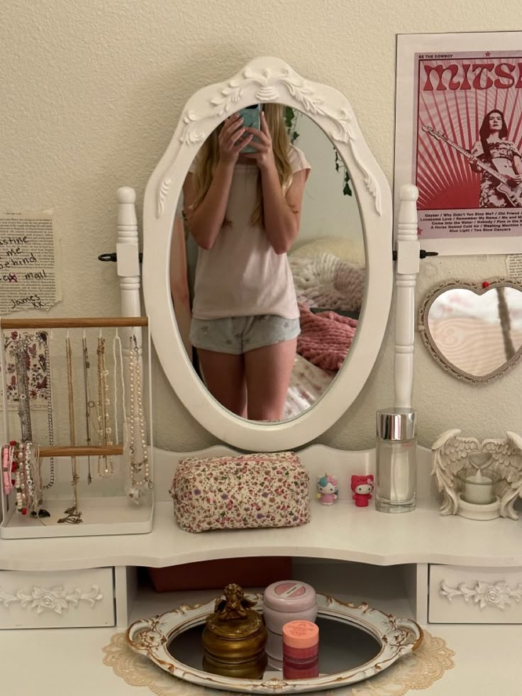 a woman taking a selfie in front of a white vanity with a mirror on it