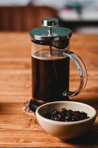 a glass coffee pot next to a white bowl with beans in it on a wooden table