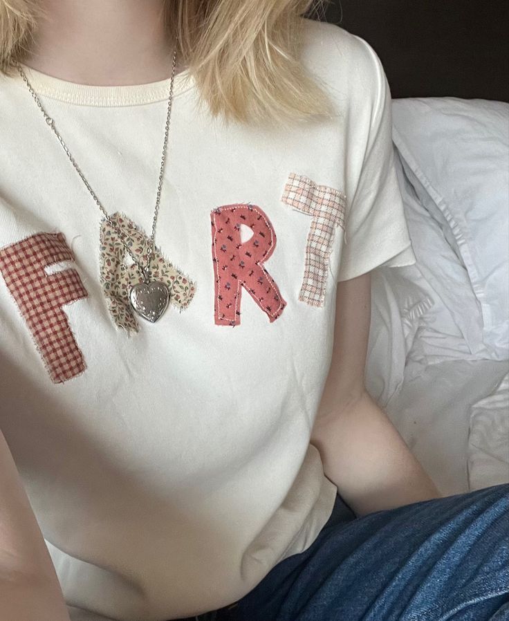 a woman sitting on a bed wearing a white shirt with the letters f and r painted on it