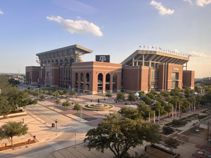 an aerial view of the outside of a stadium with trees in front and people walking around