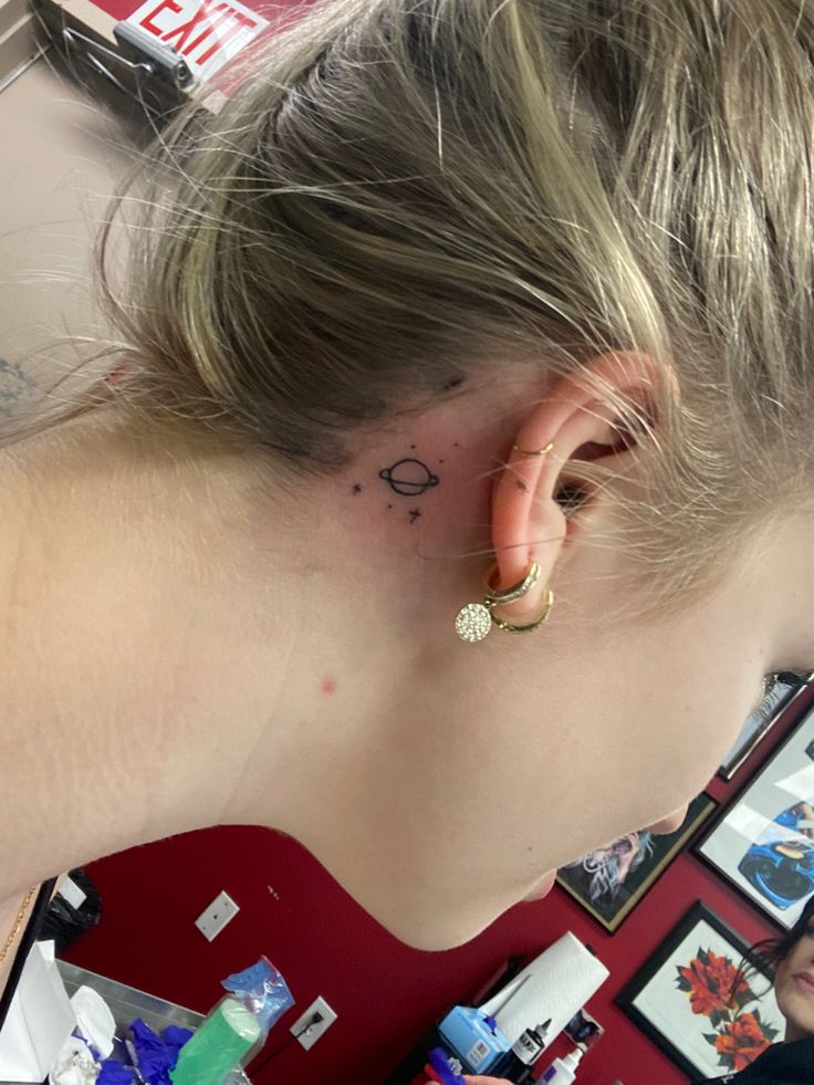 a woman with a small tattoo on her left ear and behind her ear is a mirror