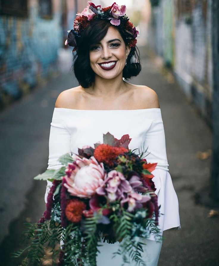 a woman with flowers in her hair is standing on the street and smiling at the camera