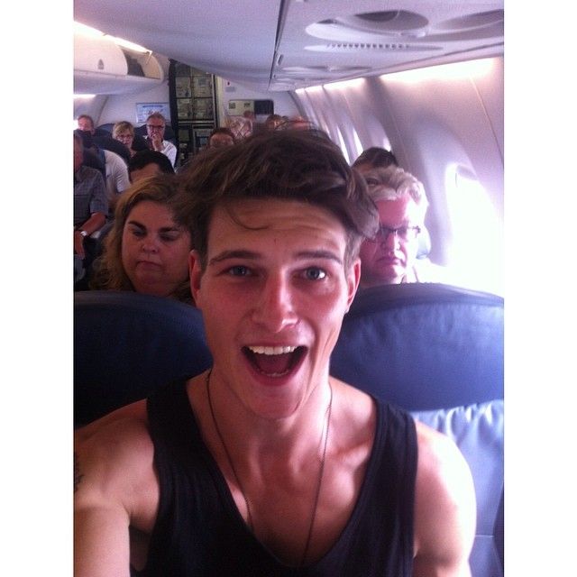 a young man with his mouth open on an airplane, surrounded by other people in the background