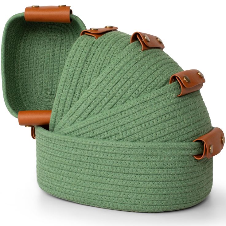 a green knitted basket with leather handles and straps on the front, sitting in front of a white background