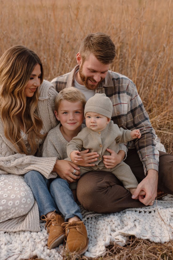 a man, woman and child sitting on a blanket in the middle of a field