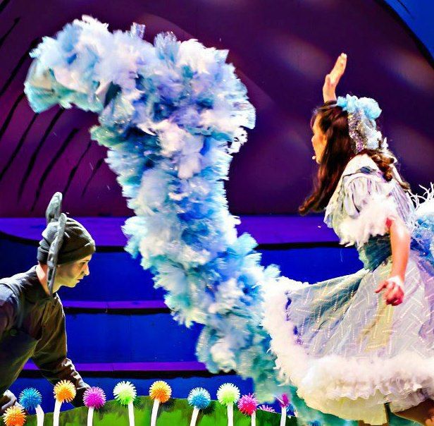 two children are performing on stage with fake flowers in front of them and one child is wearing a feathered dress