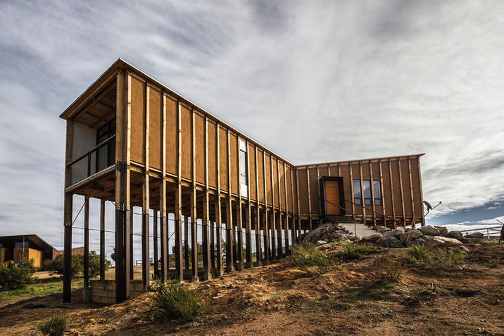 a wooden structure sitting on top of a dry grass covered hillside next to a building