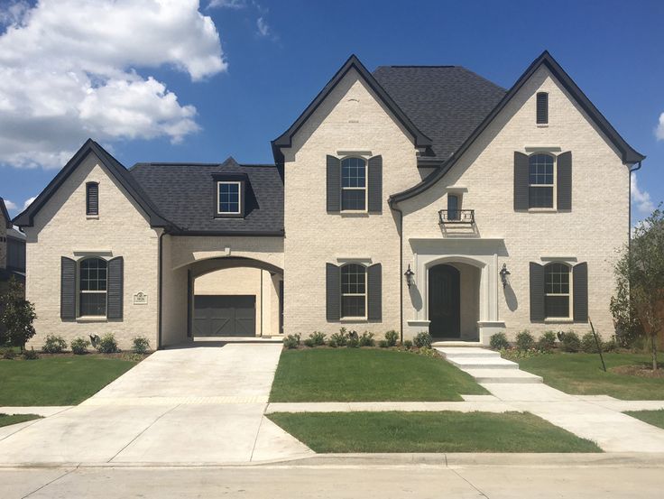 a white brick house with black shutters on the front and side windows, grass in front