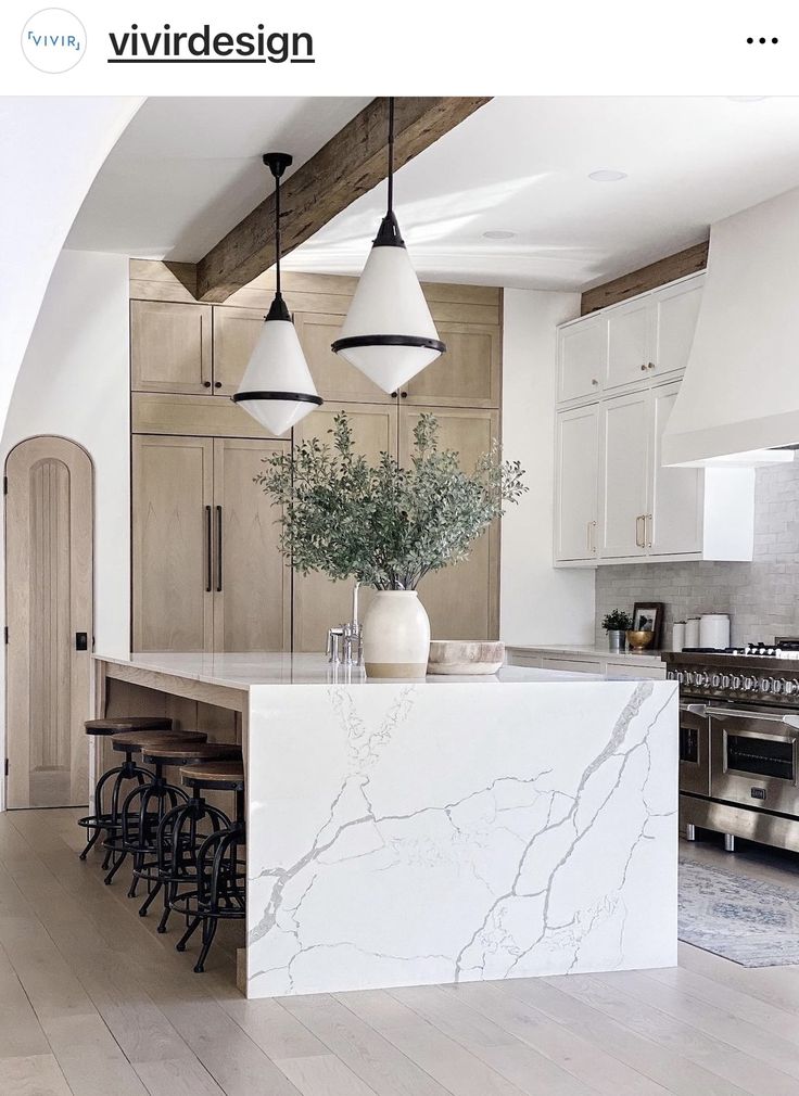 a kitchen with white marble counter tops and wooden cabinets, hanging lights over the island