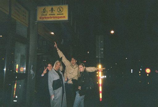 three people are standing on the sidewalk at night with their arms in the air and one person is holding his hand up