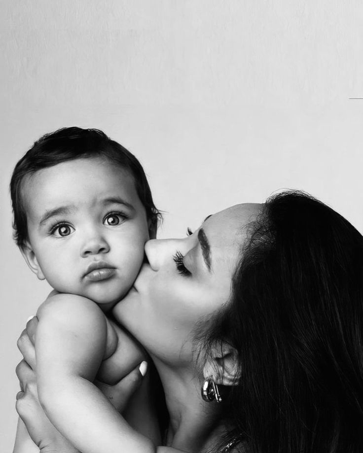 a woman is holding a baby and kissing her face with the other arm around her