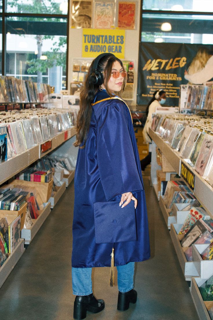 a woman in a blue graduation gown is looking at cd's and cdshelves