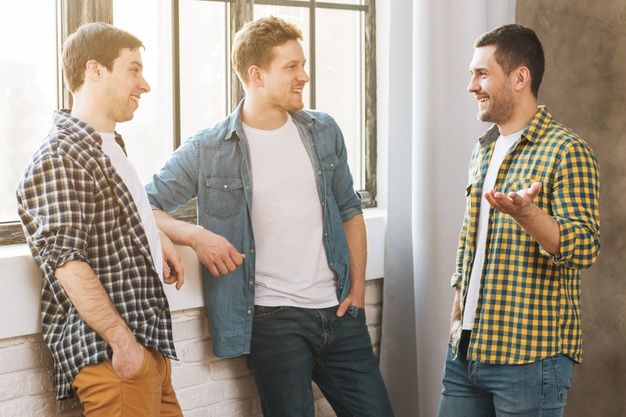 three men standing next to each other in front of a window looking at one another