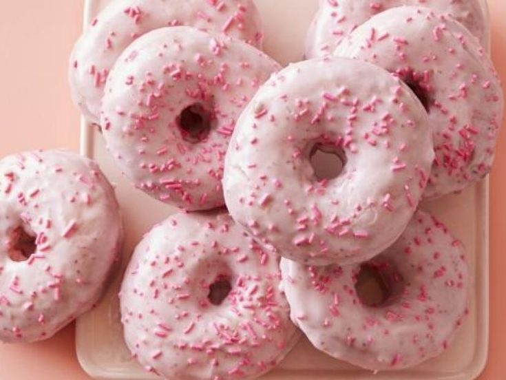 pink sprinkled doughnuts in a white tray on a pink table top