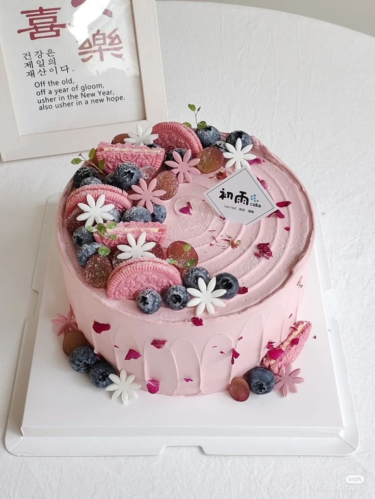 a pink cake with blueberries, strawberries and flowers on it sitting on a white plate