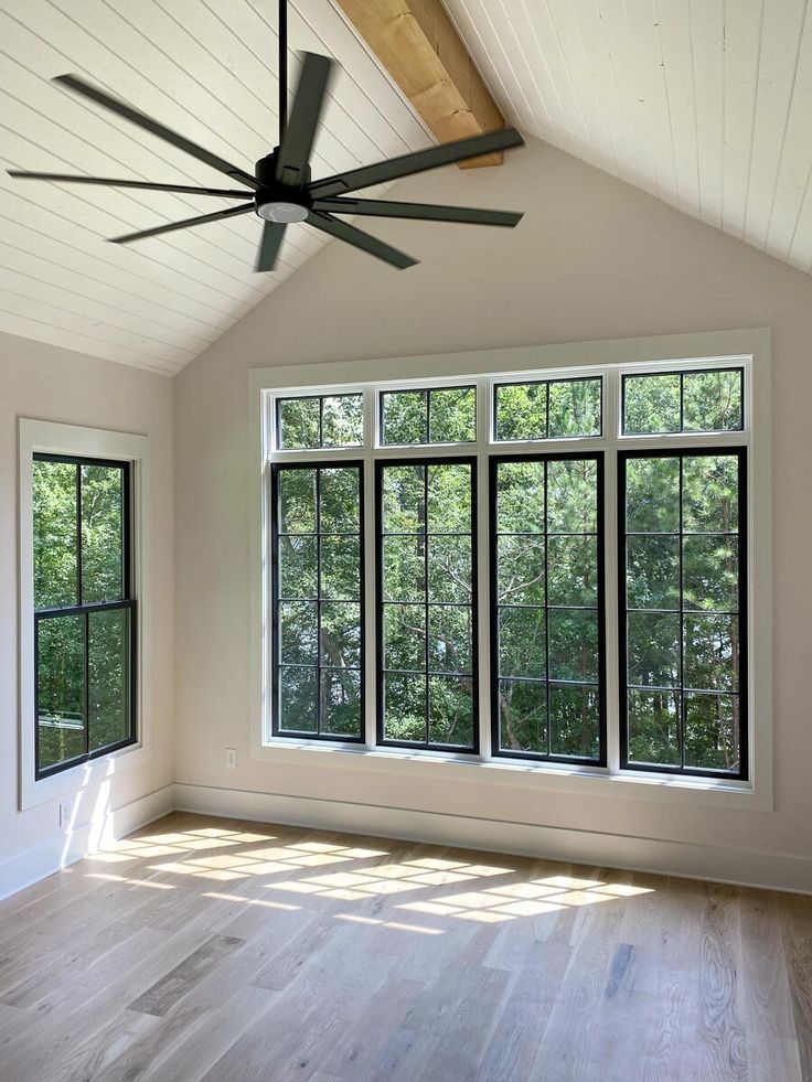 an empty room with three windows and a ceiling fan in the middle of the room