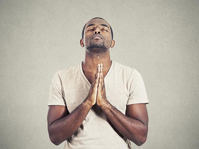 a man standing in front of a gray wall with his hands folded up to pray