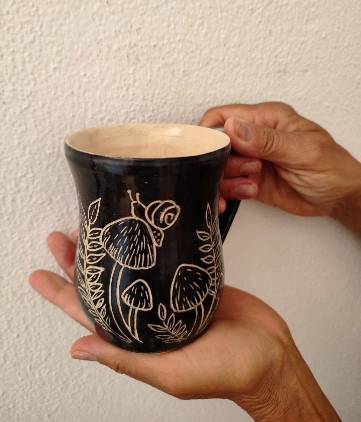 two hands holding a black and white coffee cup with designs on the outside, in front of a white wall