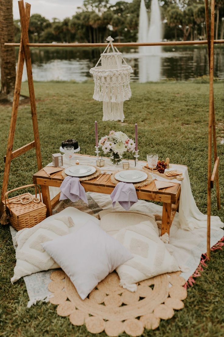 a picnic table with plates and drinks on it in the grass next to a lake