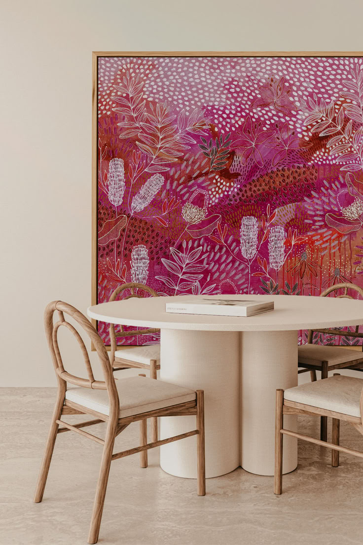 a table and chairs in front of a painting on the wall with pink flowers behind it