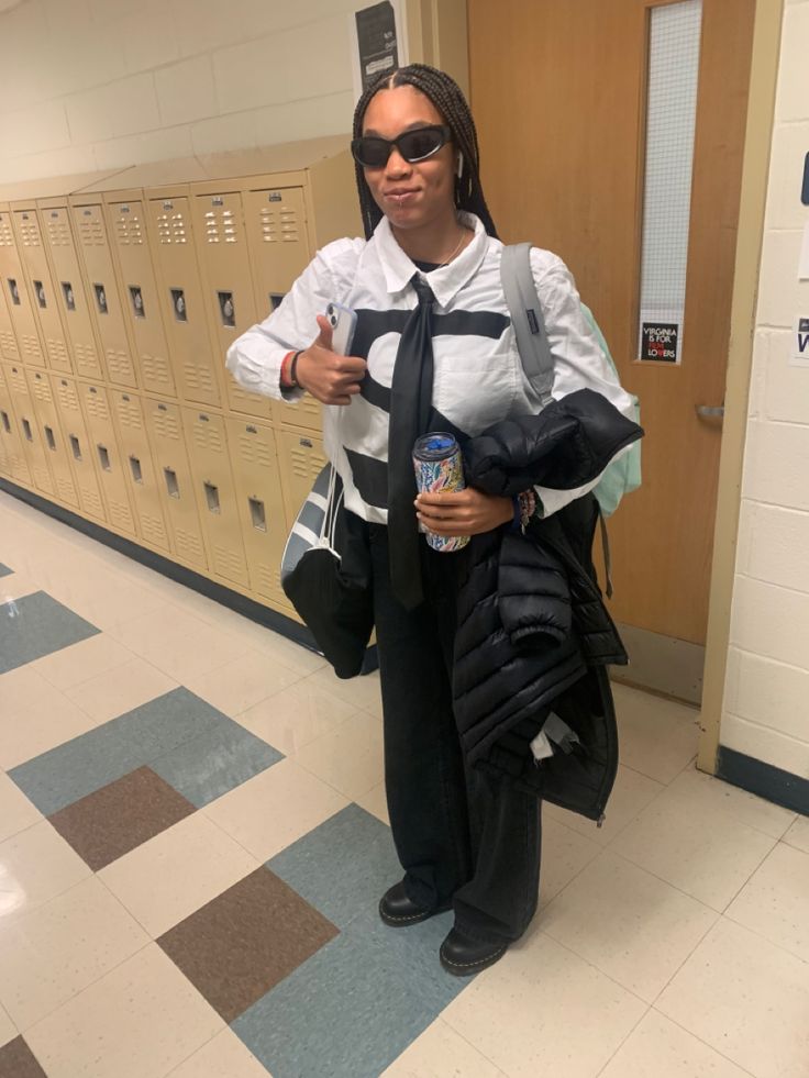 a woman with sunglasses and a tie standing in front of lockers holding a drink