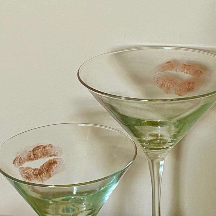 two martini glasses with lipstick imprints on the bottom and one glass filled with liquid