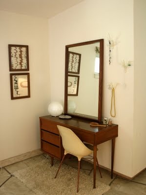 a desk with a mirror, chair and lamp in a room that has two pictures on the wall