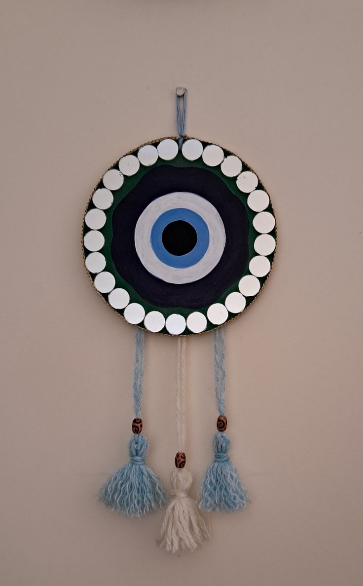 an evil eye wall hanging with tassels and beads on the bottom half of it