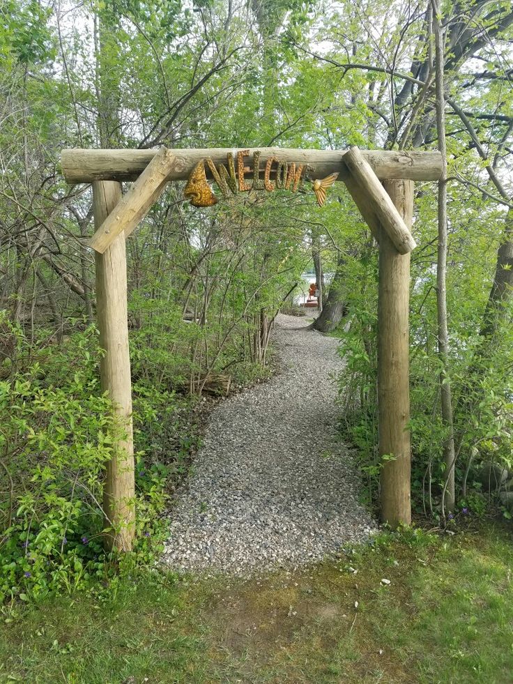 a wooden arch in the middle of a wooded area with gravel and rocks underneath it