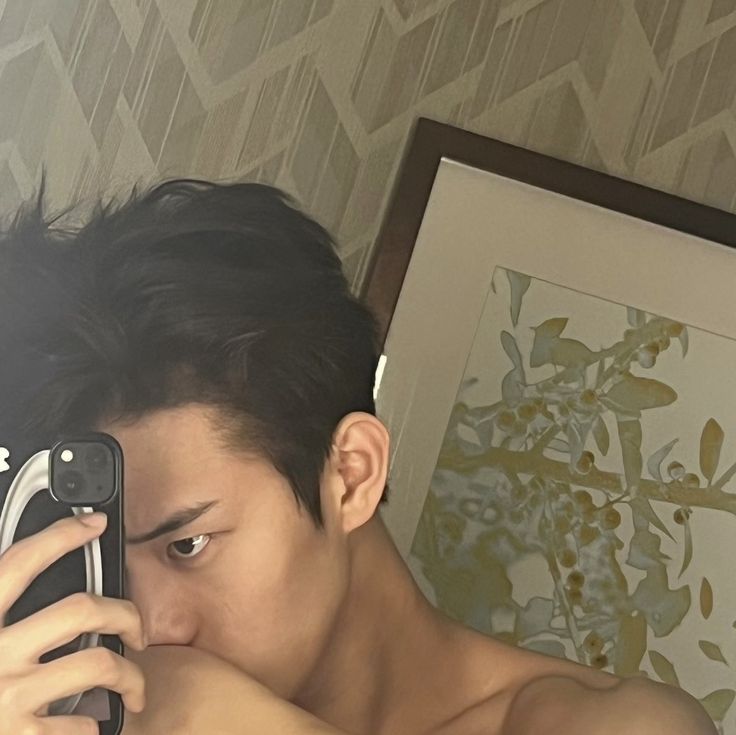 a young man taking a selfie with his cell phone in front of him while wearing no shirt