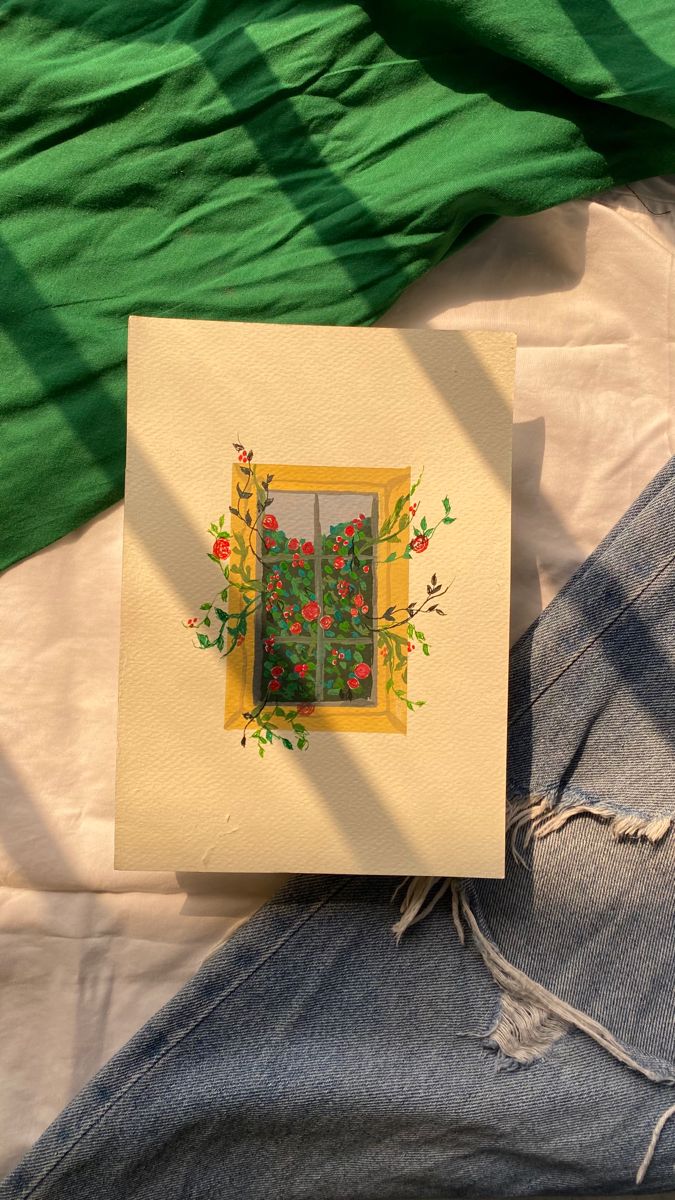 a card with an image of a window and flowers on it sitting next to a pair of jeans