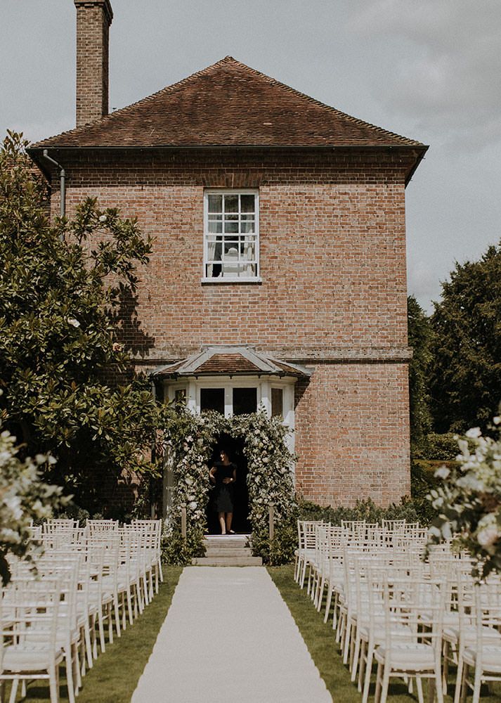 an outdoor ceremony with white chairs set up in front of a brick building and trees