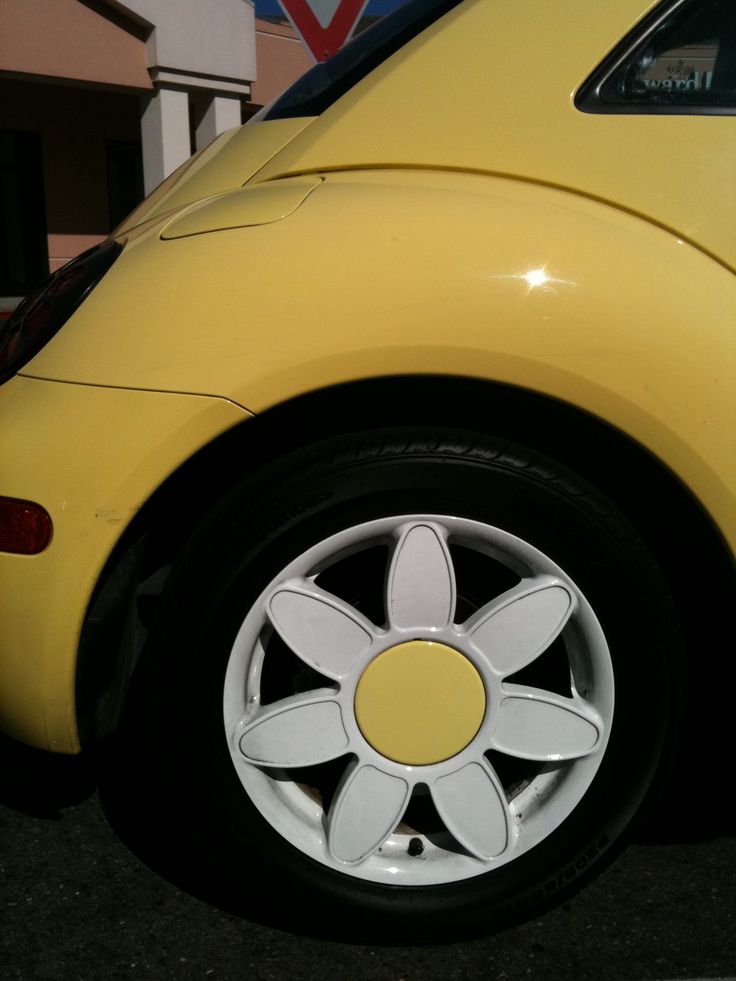 a yellow car with white spokes parked in a parking lot next to a building