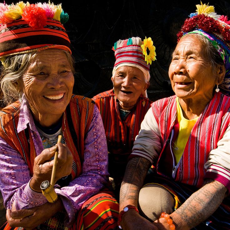 three women wearing colorful headdresses sitting next to each other on the ground