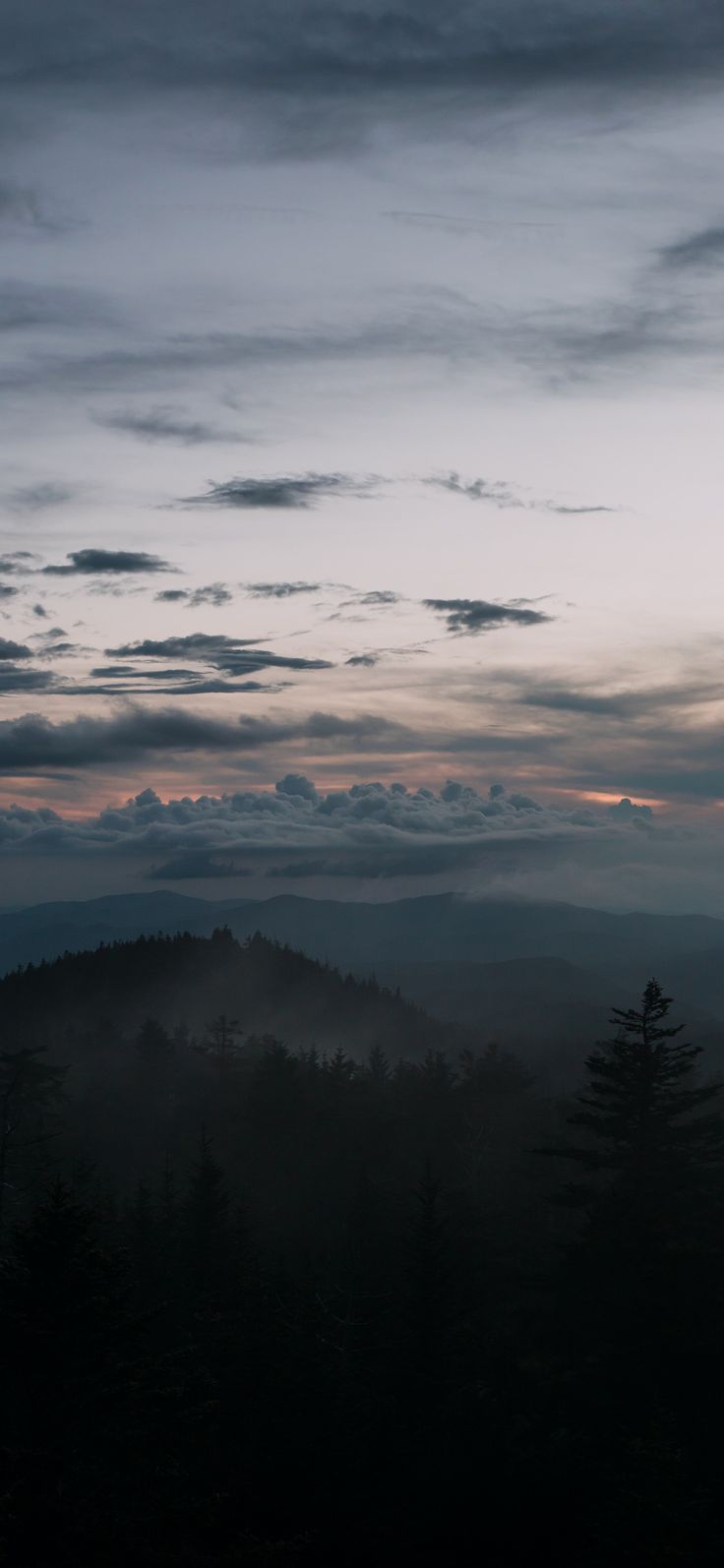 the sky is dark and cloudy with some clouds in it as the sun sets over mountains