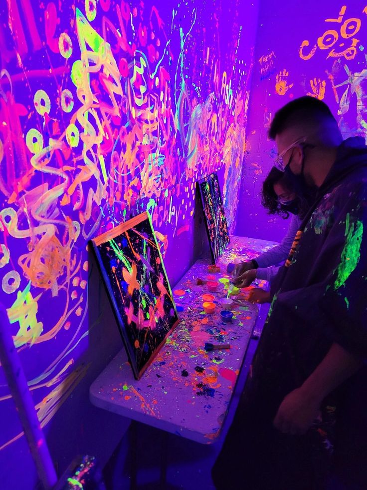 a man standing in front of a painting on a table with neon paint all over it