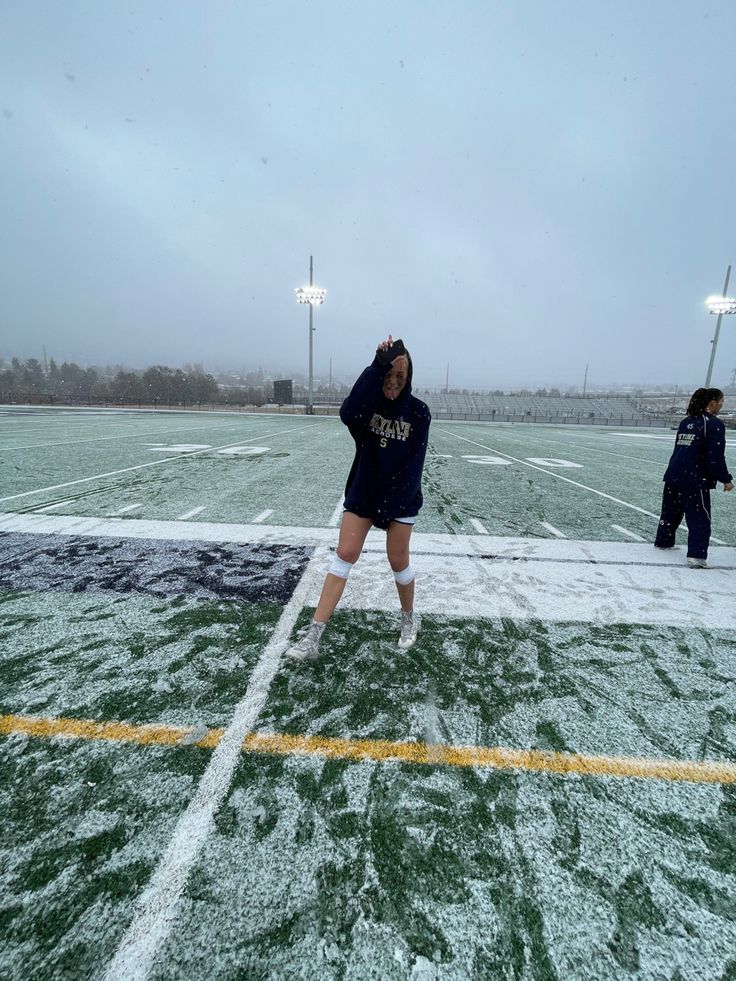 two people standing on a football field covered in snow and ice as one person takes a photo